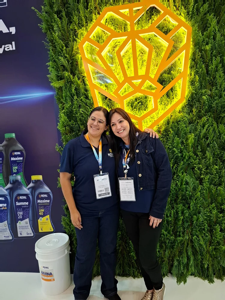Duas profissionais em estande de feira, ao lado de produtos expostos