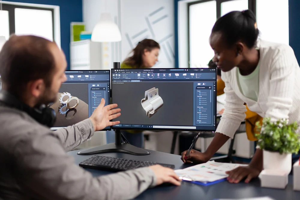 Três profissionais diante de dois monitores com software de modelagem 3D de um produto